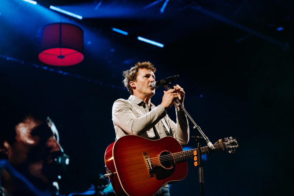 James Blunt with a guitar singing into a microphone on a stage